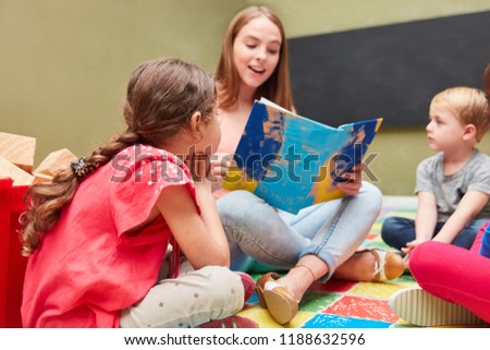 Childminder and children reading from a children's book in a kindergarten