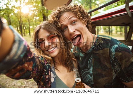 Photo of lovely hippie couple man and woman smiling and taking selfie in forest near retro minivan