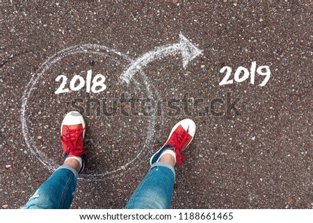 Start new year 2019 and leaving behind old year. Feet  in red sneakers standing inside 2018 year circle and outward arrow on the 2019 year chalky on the asphalt. Concept for success and passing time. Royalty-Free Stock Photo #1188661465