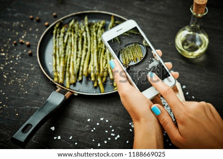 woman's hands are holding the phone and taking a picture of delicious young asparagus on a wooden table