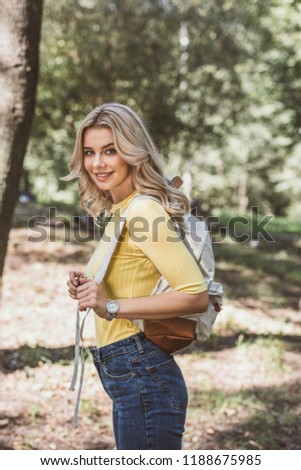side view of beautiful smiling woman with backpack in park