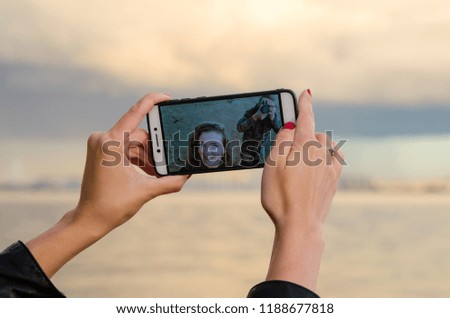 A young smiling curly girl and photographer on the mobile's phone screen during photographing and taking selfie. Darkening effect.