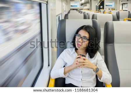 Picture of pensive business woman is holding a glass of coffee while sitting in the airport train