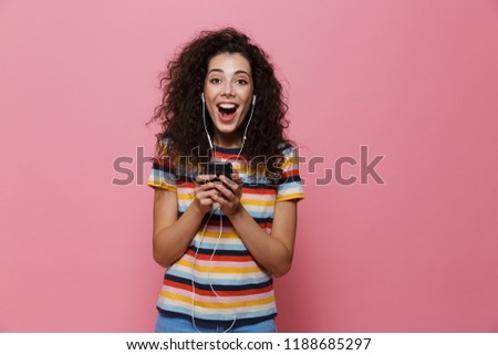 Image of an excited happy cute young woman posing isolated over pink background using mobile phone listening music.
