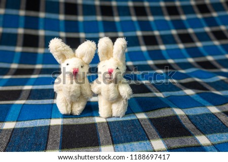 a rabbit figure, two toy rabbits, a toy rabbit, a soft toy, a white rabbit on a blue background, an Easter rabbit, a blue checkered background, a series
