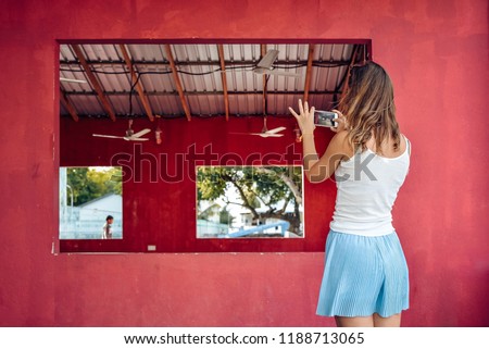 young woman makes a photo of empty pink house with a big windows using her smartphone. Maafushi island, Maldives.