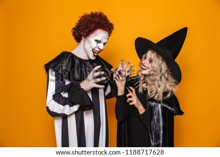 Image of witch woman and joker man wearing black costume and halloween makeup playing around isolated over yellow background