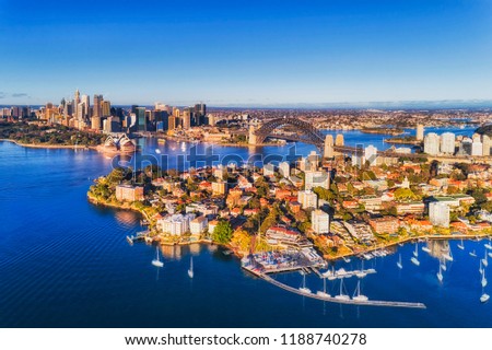 Rich blue waters of Sydney harbour reflecting clear blue sky around major Sydney city landmarks seen from above over Kirribilli yacht club towards the Sydney Harbour bridge.
