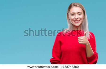 Young blonde woman wearing winter sweater over isolated background doing happy thumbs up gesture with hand. Approving expression looking at the camera with showing success.