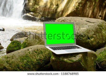 Computer laptop with green screen display set near waterfall.