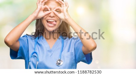 Young arab doctor surgeon woman over isolated background doing ok gesture like binoculars sticking tongue out, eyes looking through fingers. Crazy expression.