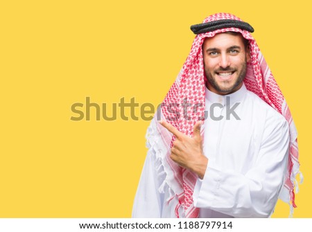Young handsome man wearing keffiyeh over isolated background cheerful with a smile of face pointing with hand and finger up to the side with happy and natural expression on face looking at the camera.