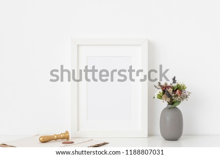 Elegant white a5 portrait frame mockup with bouquet of dried flowers in gray vase and gold stamp on white wall background. Empty frame, poster mock up for presentation design. Template frame for text