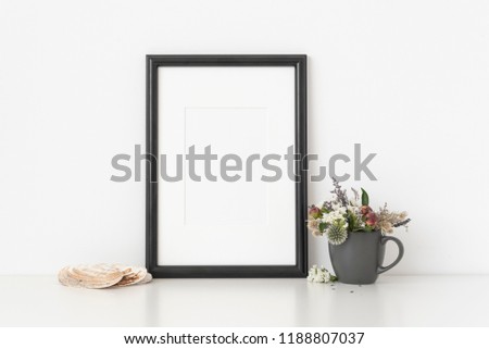 Black a4 portrait frame mockup with dried field wild flowers in vase and seashells on white wall background. Empty frame, poster mock up for presentation design. Template frame for text, lettering