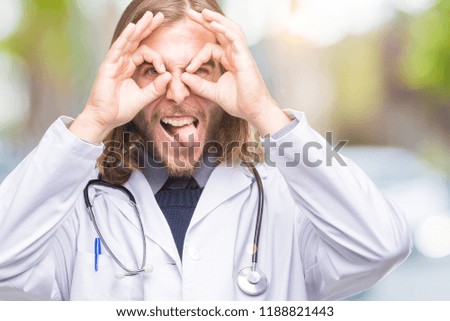 Young handsome doctor man with long hair over isolated background doing ok gesture like binoculars sticking tongue out, eyes looking through fingers. Crazy expression.
