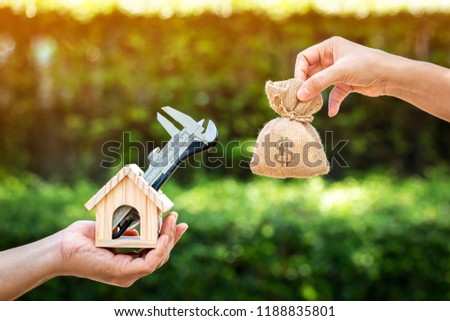 Women and man hand holding a wooden home with repairing and a money bag put together on sunlight in the public park, Saving money and loan for construction real estate and house concept.