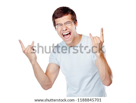Young excited man wearing glasses and blue t-shirt showing horns hand gesture with both hands and happy screaming isolated on white background - joy concept