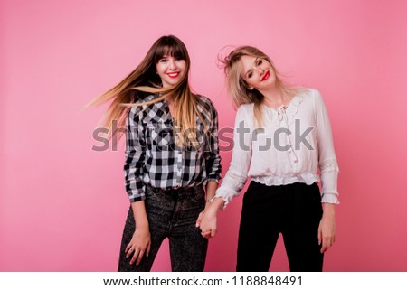 Two playful women jumping and having fun in studio on pink background.  Windy hairs. Positive mood. 