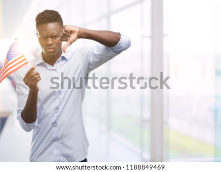 Young african american man holding USA flag with angry face, negative sign showing dislike with thumbs down, rejection concept
