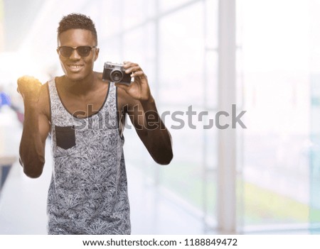 Young african american man holding vintage camera screaming proud and celebrating victory and success very excited, cheering emotion