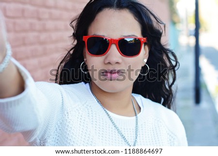 Portrait of beautiful young latin woman with sunglasses making selfie. Outdoors. 