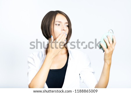 beautiful girl yawns with an alarm clock, short haircut, isolated on a white background