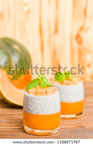 Chia pudding with pumpkin puree in beautiful glasses with green mint leaves and fresh ripe vegetable on brown wooden background - raw vegetarian sweet healthy organic dessert.