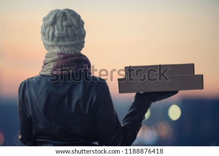 A girl in winter clothes with a box for pizza on the background of the evening city. 24 hours delivery. Concept