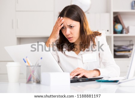 Tired young girl manager with laptop and documents  working at office table