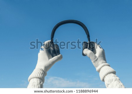 Female hands in the winter mittens with a headphones on the cloudy blue sky. Concept