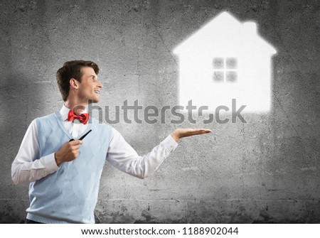 Confident and young businessman smoking pipe and drawn house on gray wall background