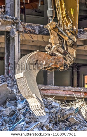 Close-up of an excavator at a demolition site, with the partially demolished building in the background
