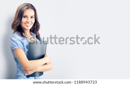 Happy businesswoman in blue confident clothing, with black folder, over grey background, with blank copy space place for advertising, slogan or text. Brunette model in business concept studio shoot.