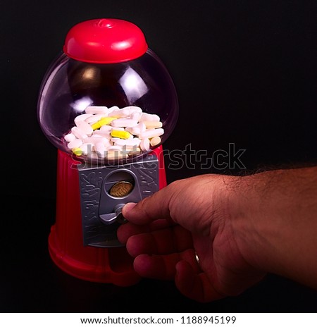 45 degrees photo of red plastic sweet machine full of pills, some of them white and some others yellow, and a hand using the wheel