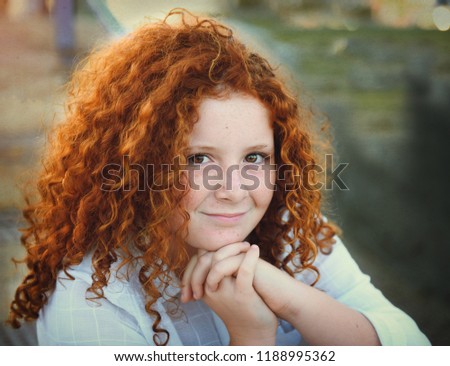 Pretty redhead young girl with curly hair portrait outdoors