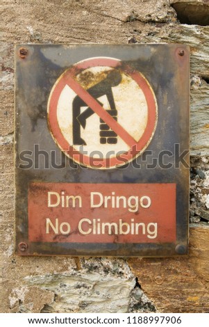 Welsh language No Climbing Dim Dringo sign on an old stone wall with symbol of man climbing on a wall in a red circle with red line through