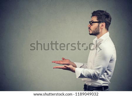 Side view of man with hands extended looking away while asking for help on gray background