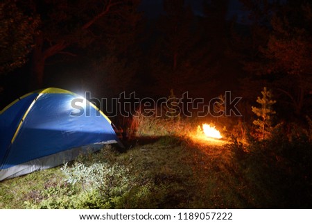 Camping at night with a tent and fire as a symbol of adventure, travel and romance.