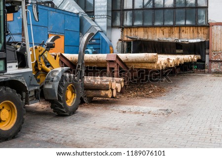 Forklift truck grabs wood in a wood processing plant. Large log loader unloading a log truck in the log yard at a conifer log mill. Processing of timber at the sawmill. Royalty-Free Stock Photo #1189076101
