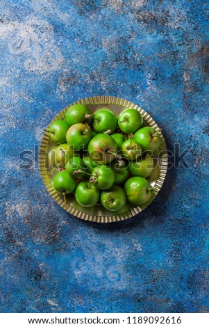 Green organic apples on silver metallic plate and blue painted background overhead fresh arrangement in studio