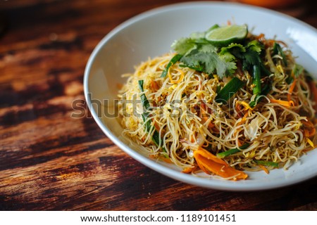 Healthy Vegetarian vegan menu Delicious Singapore style Stir fried rice noodles with carrot orange smoothies on wooden table in cafe Royalty-Free Stock Photo #1189101451