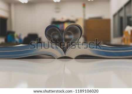 Open book with heart shape page on table and blurred bookshelf. Education background.