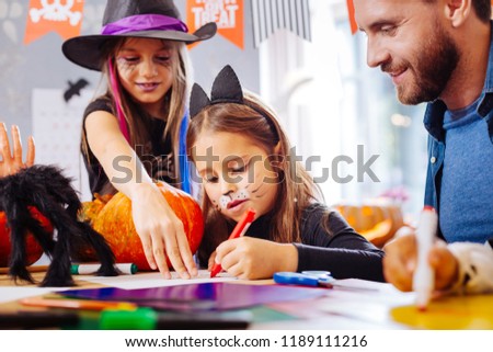 Funny face. Cute little girl wearing cat Halloween costume having funny painted face while coloring pictures