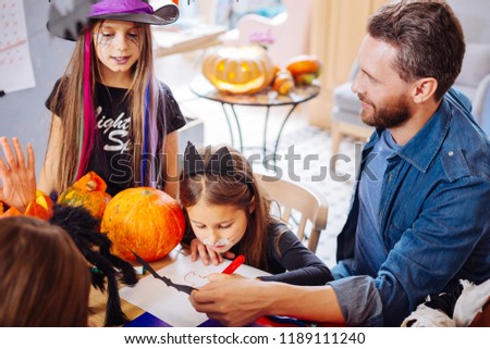 Father and daughters. Loving beaming handsome father helping his daughters coloring pictures for Halloween