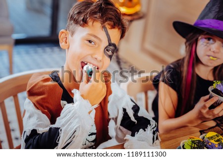 Gummy eye. Handsome dark-eyed boy wearing pirate suit for Halloween feeling excited while eating gummy eye