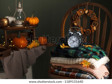 Fall is here,  autumn time, colorful tartan plaids woolen textile on wooden stool chair, fall wreath, alarm clock rustic black background
