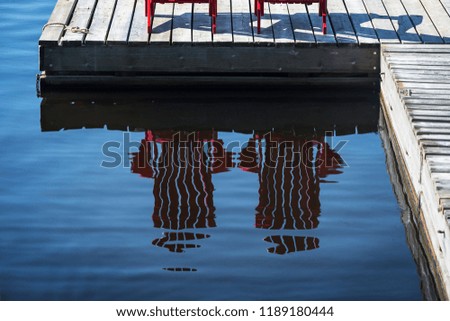 Two red Adirondack chairs reflected in the wavy water