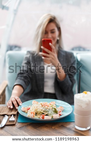 Young beautiful happy girl eats and makes a photo of food on the phone in a restaurant. Concept food photo.