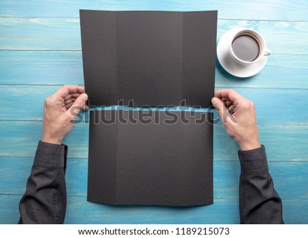 Mens hands holding empty black booklet on blue wooden background. View from above