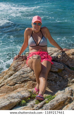 A beautiful girl poses on a rock in front of the sea